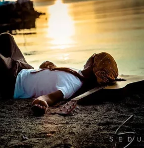Lee Sharp laying on beach with guitar